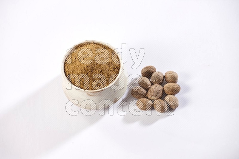 A beige pottery bowl full of nutmeg powder with the seeds beside it on a white flooring in different angles