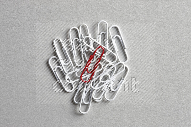 A bunch of white paper clips with a different colored paper clip in the center on grey background
