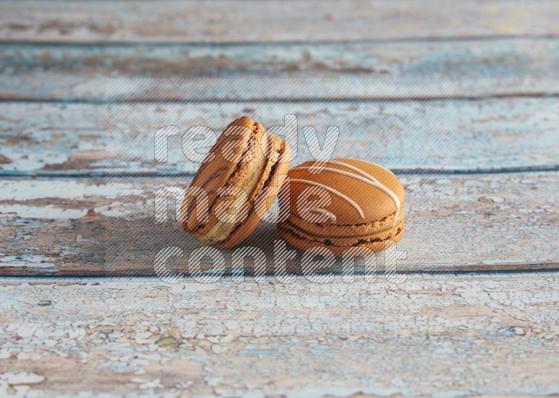 45º Shot of of two assorted Brown Irish Cream, and light brown Almond Cream macarons next to each other on light blue background