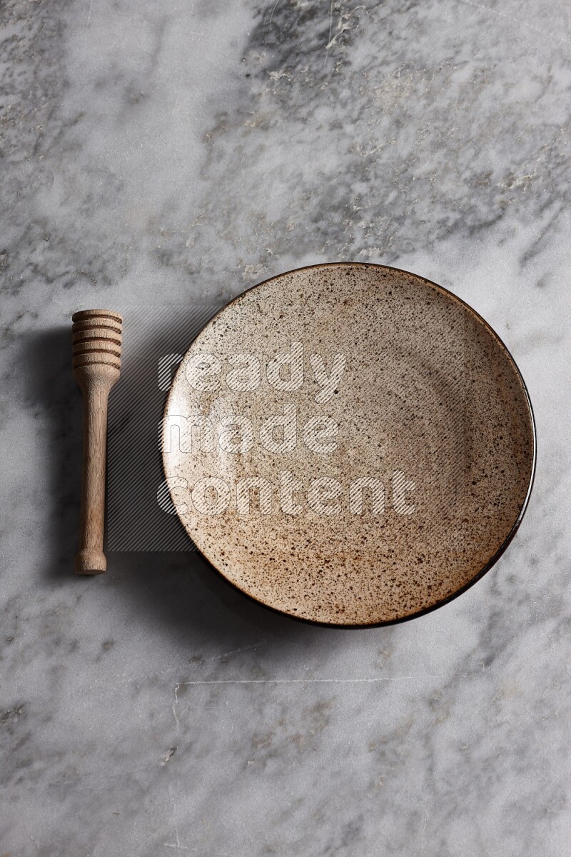 Multicolored pottery plate with wooden honey dipper on the side on grey marble background