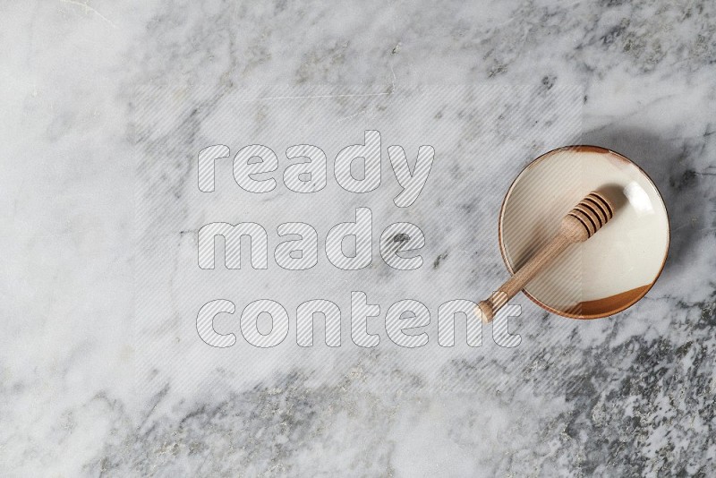 Multicolored Pottery Plate with wooden honey handle in it, on grey marble flooring, Top View