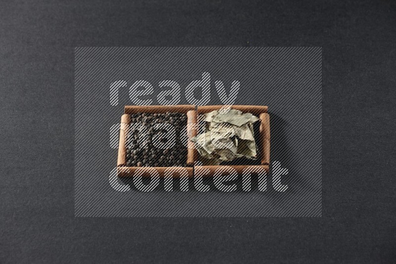 مربعان من أعواد القرفة ممتلئان بحبوب الفلفل الأسود وأوراق الغار علي خلفية سوداء