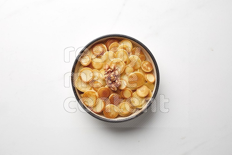 Top-view shot of walnut cereal pancakes in a round bowl on white background