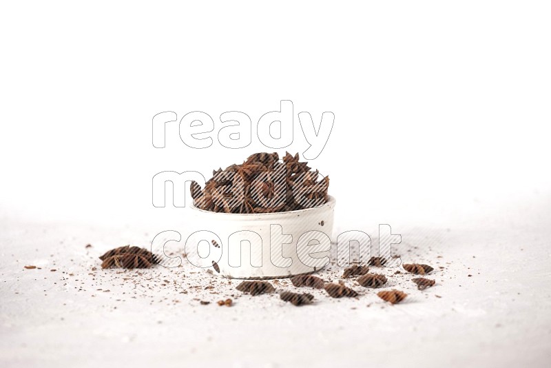 Star Anise in a white bowl and more of it sprinkled on white background