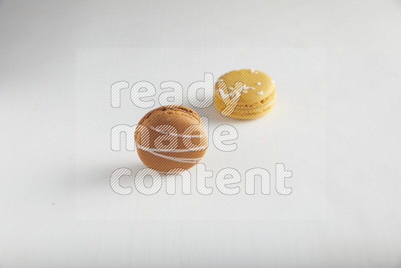 45º Shot of of two assorted Brown Irish Cream, and Yellow Piña Colada macarons on white background
