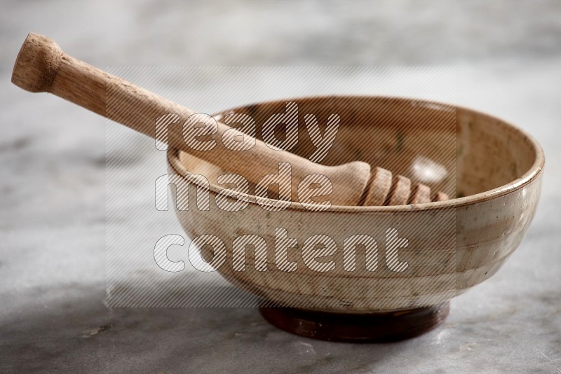 Beige Pottery bowl with wooden honey handle in it, on grey marble flooring, 15 degree angle