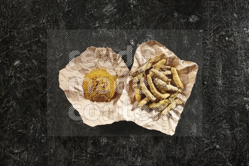 أصابع الكركم المجففة وبودرة الكركم في قطع من الورق على خلفية سوداء