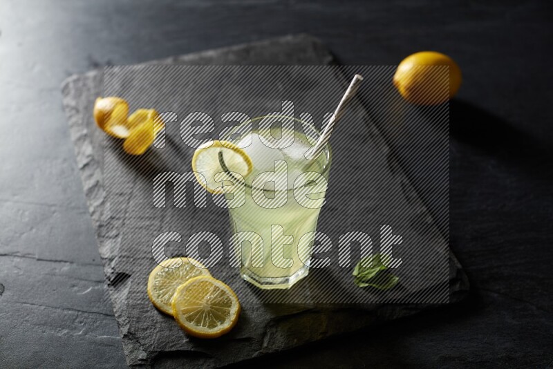 A glass of lemon juice with a straw on black background
