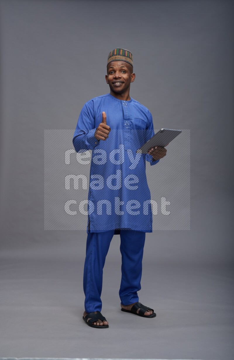 Man wearing Nigerian outfit standing working on tablet on gray background