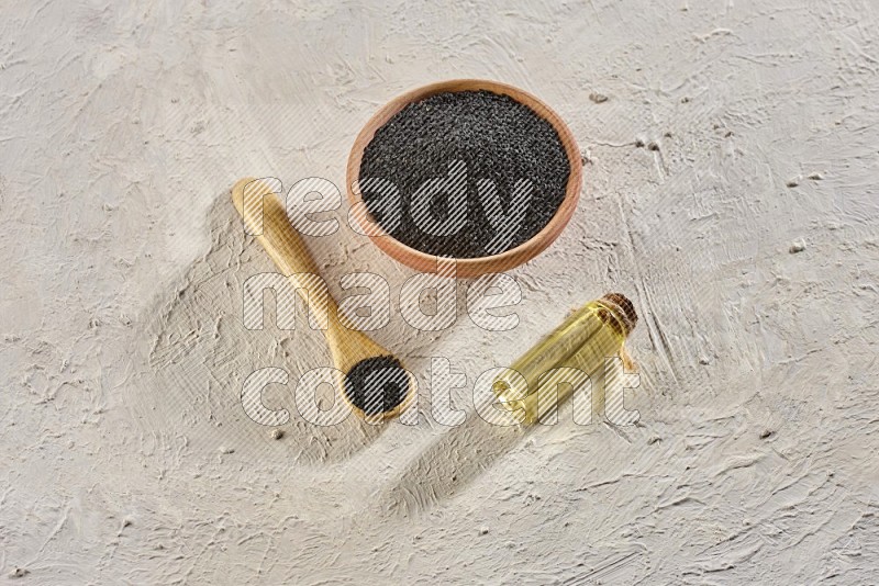 A wooden bowl and spoon full of black seeds and a bottle of black seeds oil on a textured white flooring in different angles