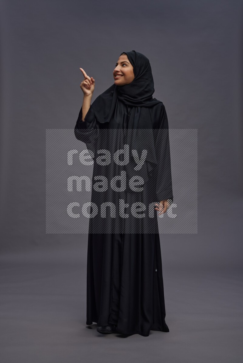 Saudi woman wearing Abaya standing interacting with the camera on gray background
