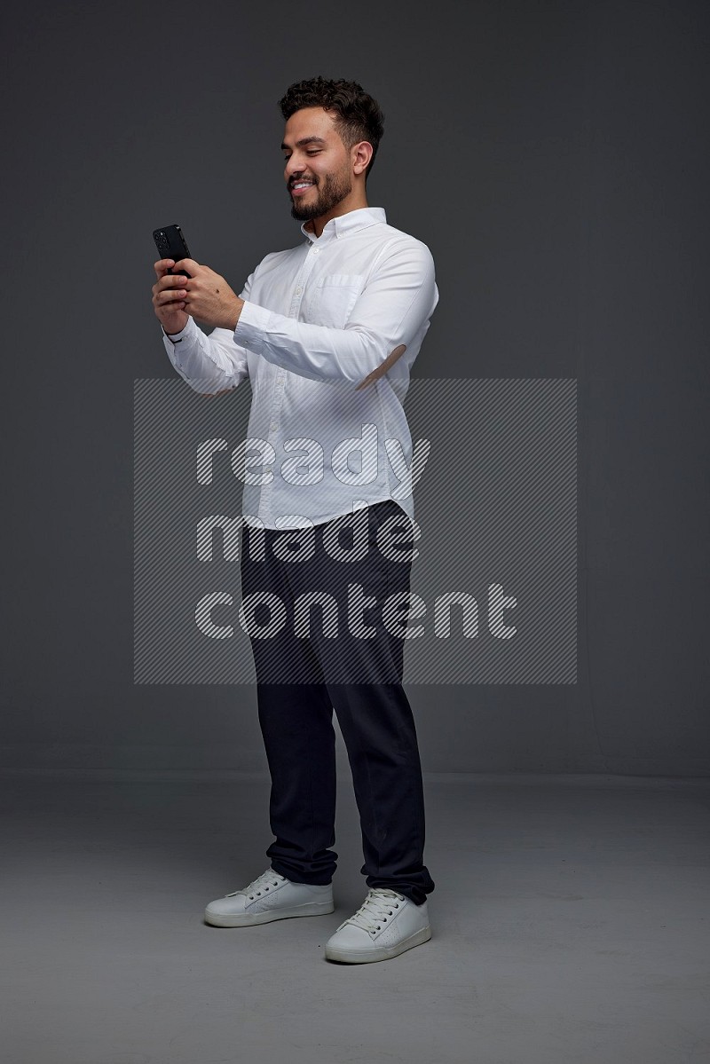 A man wearing smart casual standing and using his phone eye level on a gray background