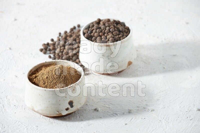 وعاءان بيج، أحدهما ممتلئ ببودرة بهار الفلفل الحلو والآخر بالحبوب مع البودرة والحبوب متناثرة على خلفية بيضاء