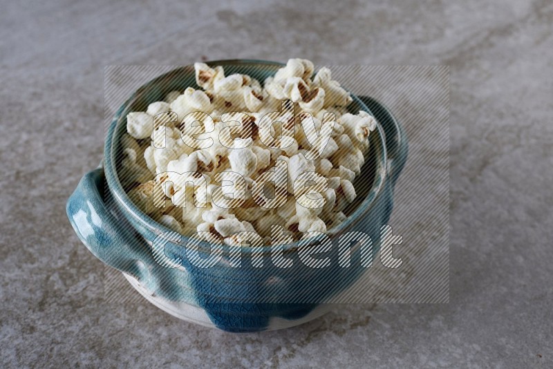 popcorn in a multi-colored handheld ceramic bowl on a grey textured countertop
