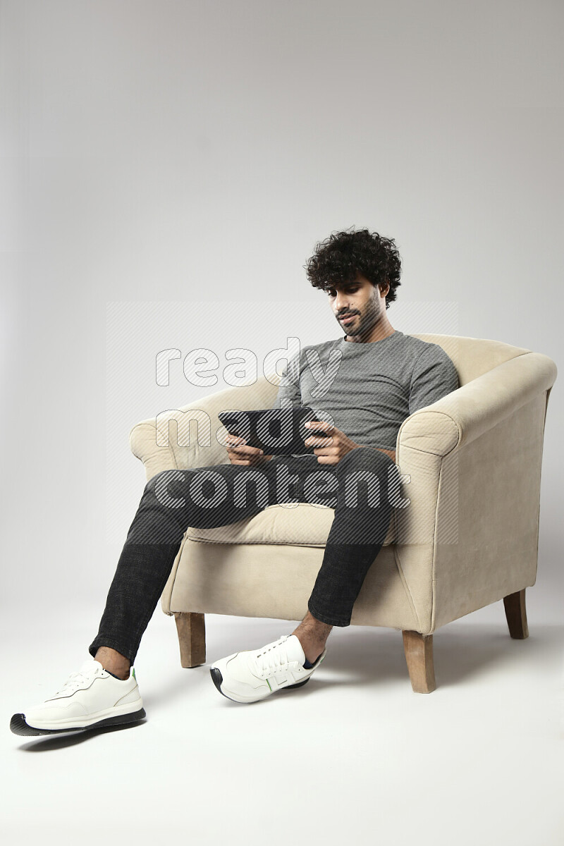 A man wearing casual sitting on a chair gaming on a tablet on white background