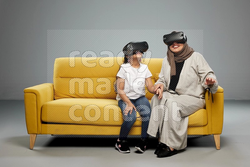 A girl and her mother sitting playing with VR on gray background