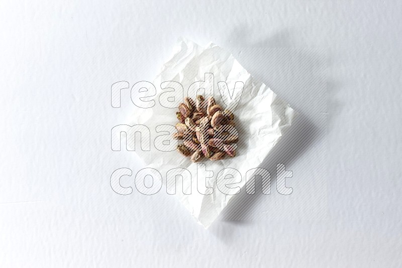Peeled pistachios on a crumpled piece of paper on a white background in different angles