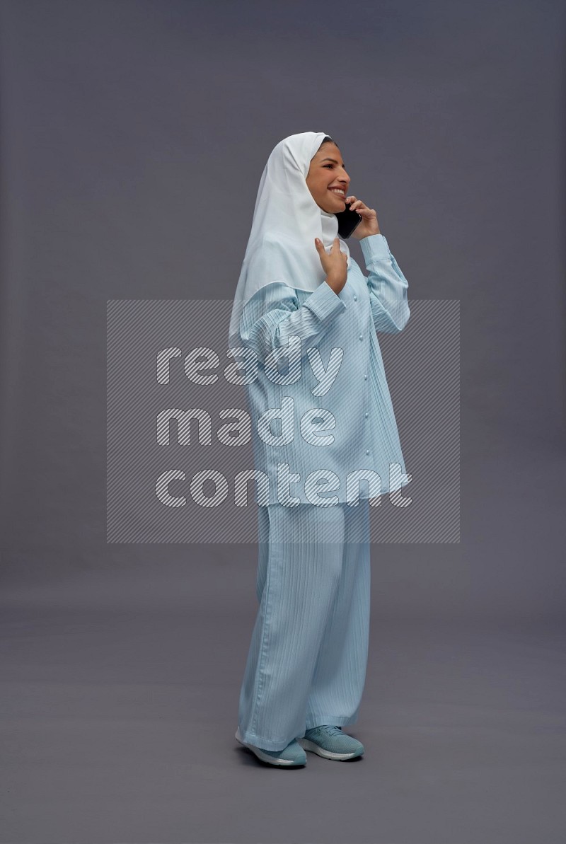 Saudi woman wearing hijab clothes standing talking on phone on gray background