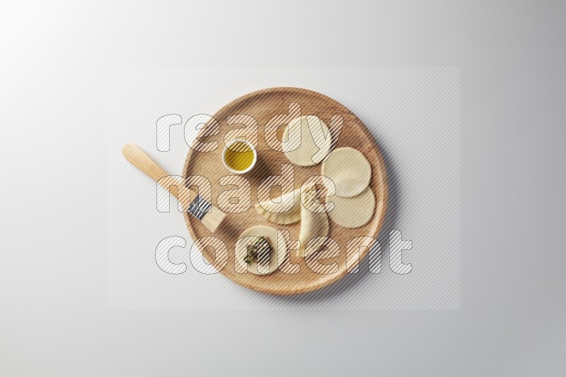 two closed sambosas and one open sambosa filled with meat while oil with oil brush aside in a wooden dish on a white background