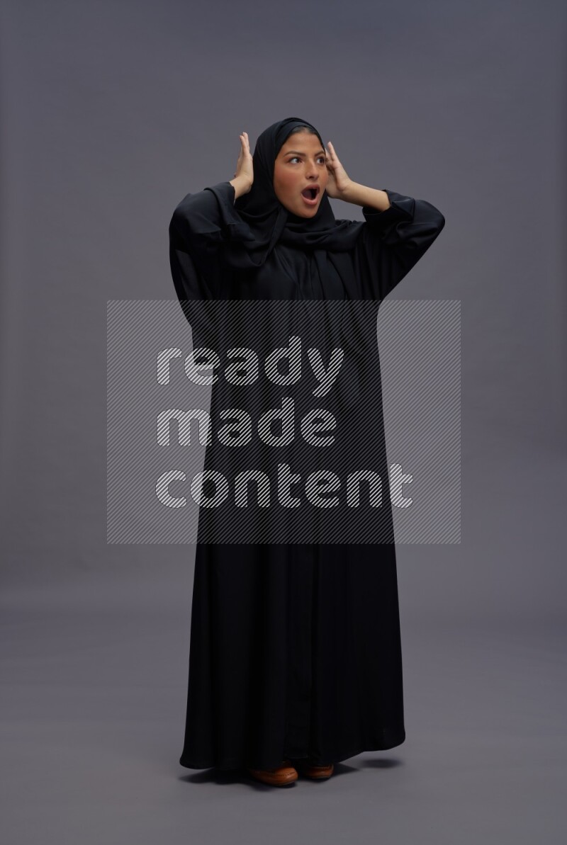 Saudi woman wearing Abaya standing hands behind head on gray background