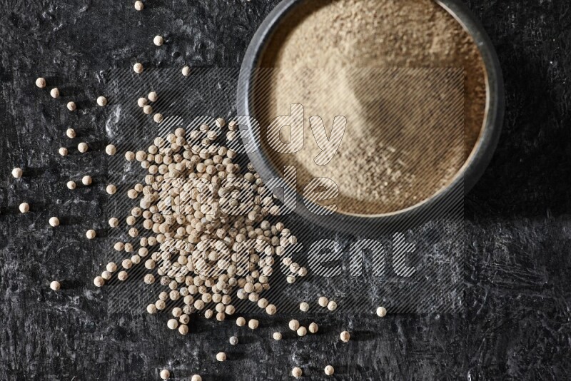 وعاء فخار أسود مملوء ببودرة الفلفل الأبيض مع حبات الفلفل الأبيض على أرضية سوداء