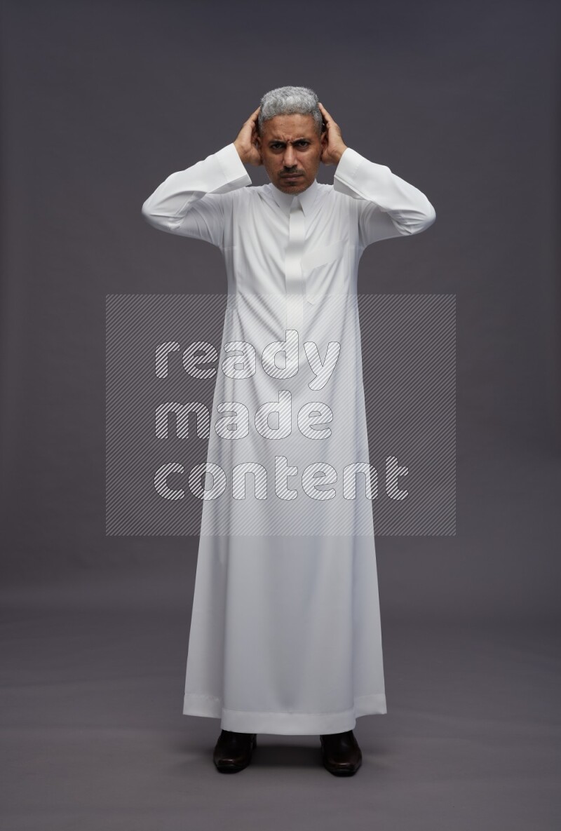 Saudi man wearing thob standing hands behind head on gray background