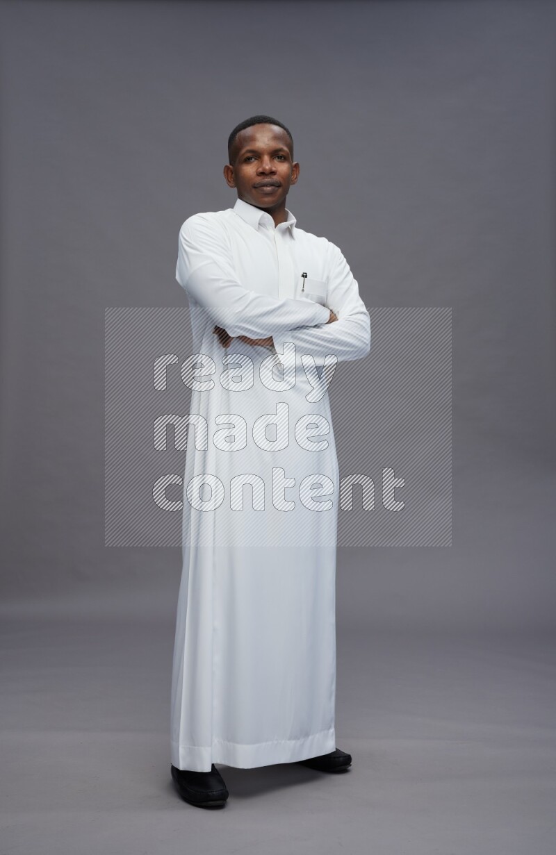 Saudi man wearing thob standing with crossed arms on gray background