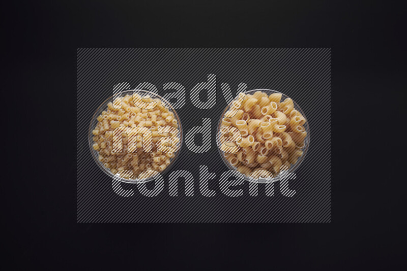Different pasta types in glass bowls on black background