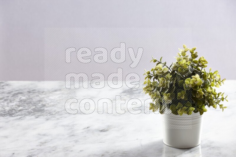 Green artificial plant in white pot on light grey marble background