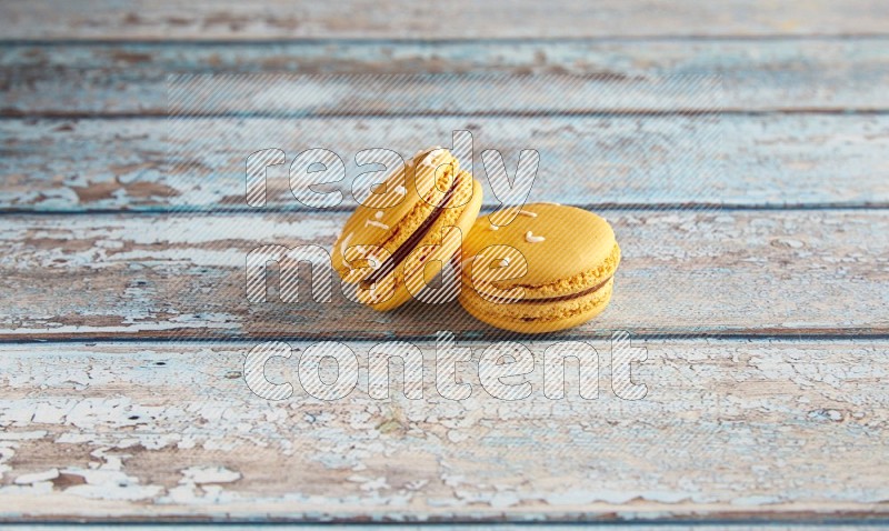 45º Shot of two Yellow Piña Colada macarons on light blue wooden background