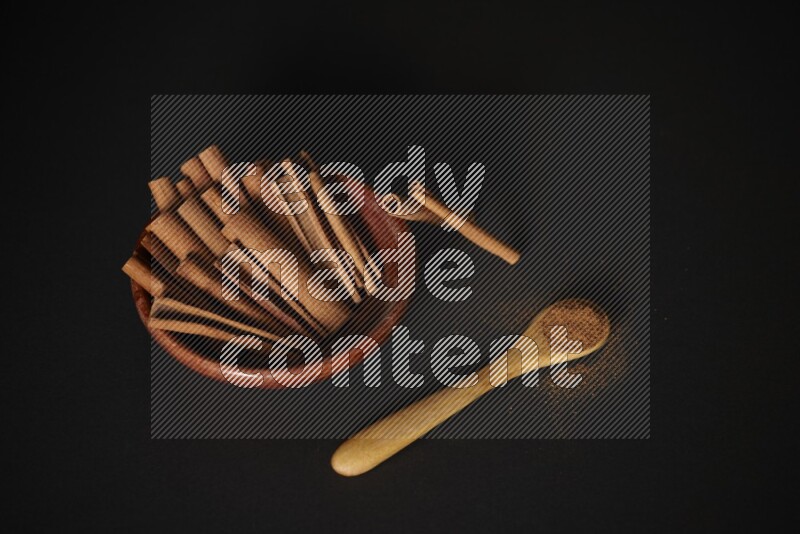 Cinnamon sticks in wooden bowl and cinnamon powder in a wooden spoon on black background