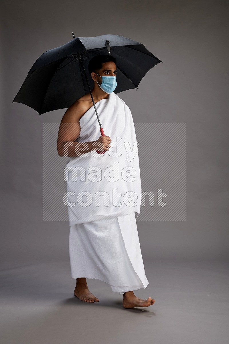 A man wearing Ehram and mask Standing holding umbrella on gray background on gray background