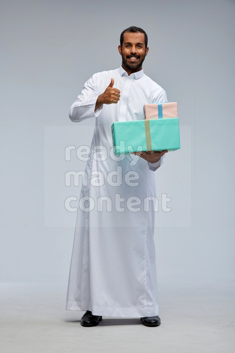 Saudi man Wearing thob standing holding gift box on Gray background