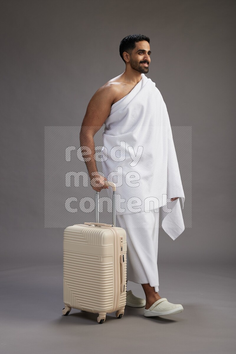 A man wearing Ehram Standing holding traveling bag on gray background