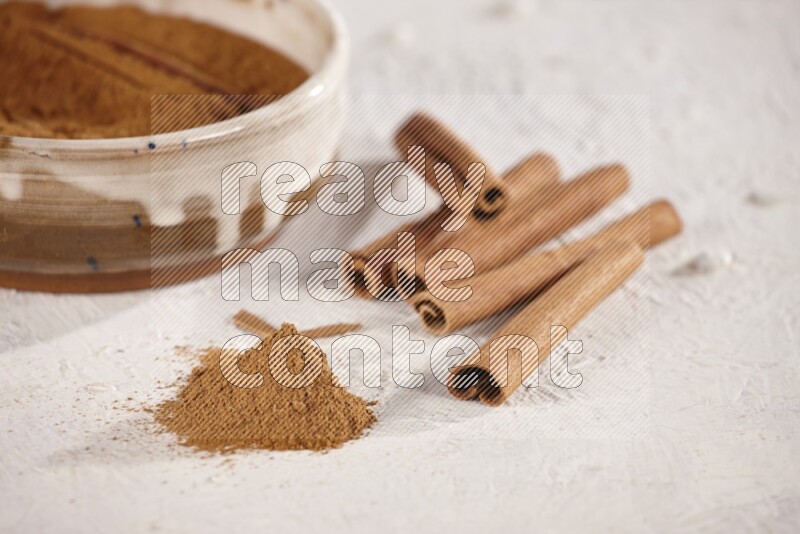 Ceramic bowl full of cinnamon powder with cinnamon sticks on the side on white background