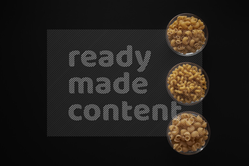Different pasta types in 3 glass bowls on black background