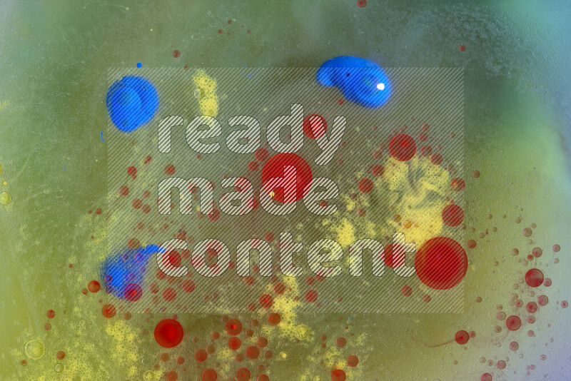 The image captures a dramatic splatter of yellow, red and blue paints over a green backdrop