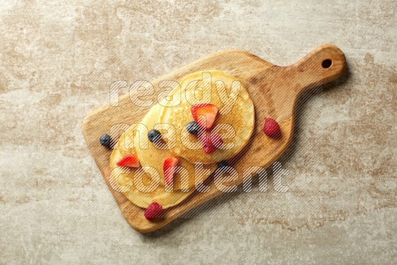 Three stacked mixed berries pancakes on a wooden board on beige background