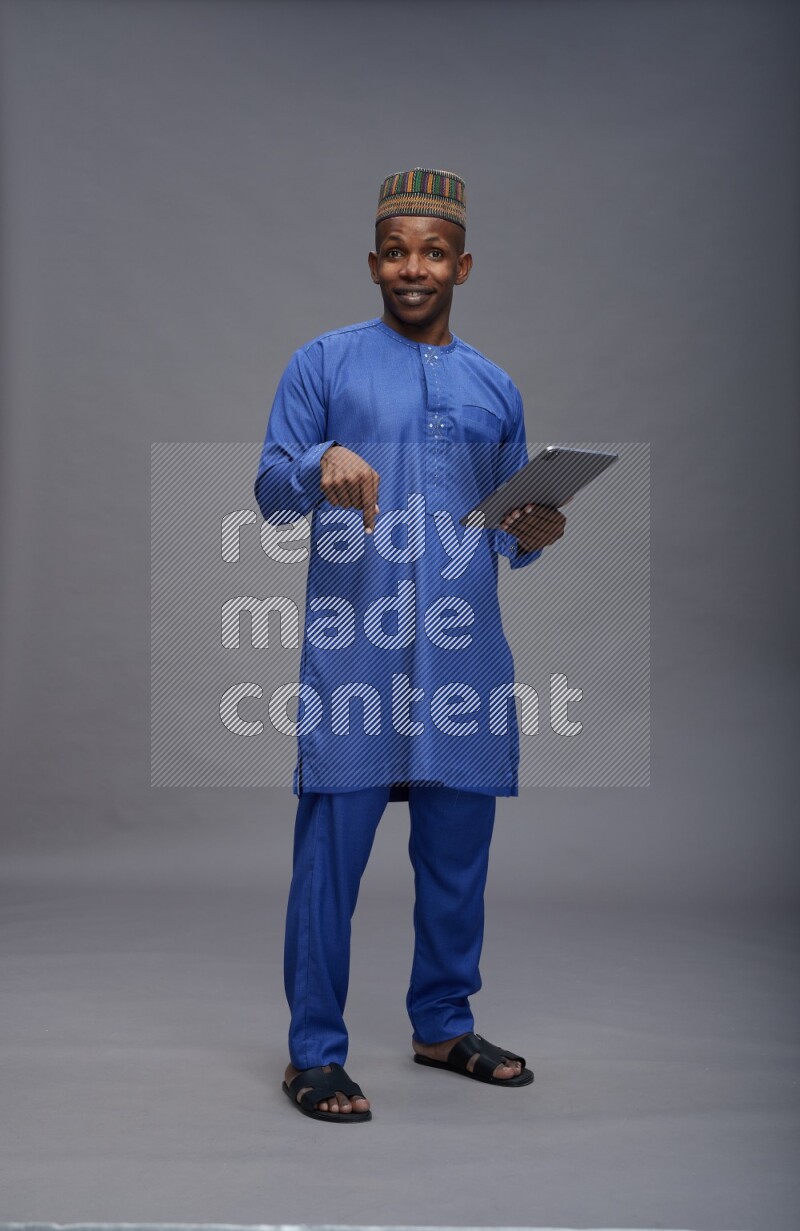 Man wearing Nigerian outfit standing working on tablet on gray background