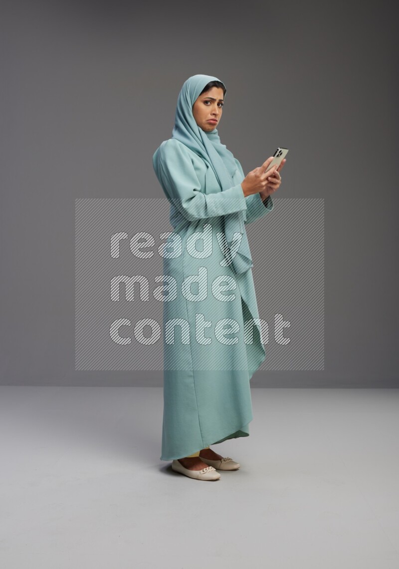 Saudi Woman wearing Abaya standing texting on phone on Gray background