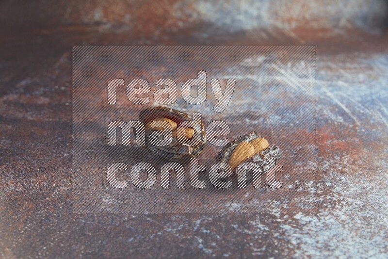 two almond stuffed madjoul dates on a rustic reddish background
