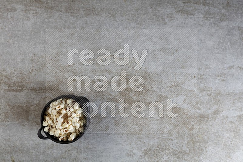 popcorn in a black handheld ceramic bowl on a grey textured countertop