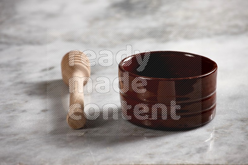 Brown Pottery bowl with wooden honey handle on the side with grey marble flooring, 15 degree angle