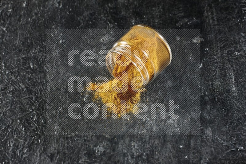 وعاء زجاجي مقلوب ممتلئ ببودرة الكركم والبودرة تناثرت منه على خلفية سوداء