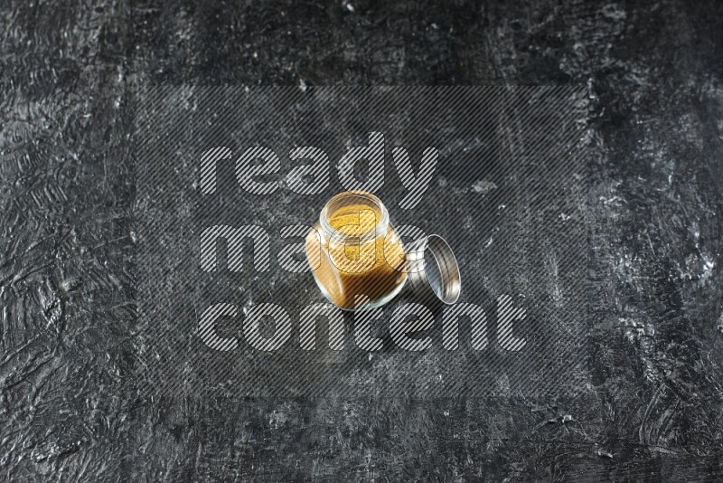 وعاء زجاجي للتوابل ممتلئ ببودرة الكركم على خلفية سوداء