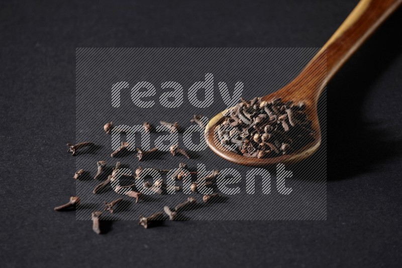 A wooden ladle full of whole cloves on a black flooring