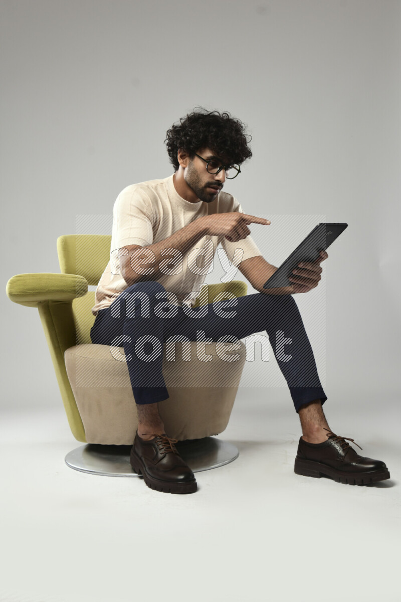A man wearing casual sitting on a chair browsing on a tablet on white background