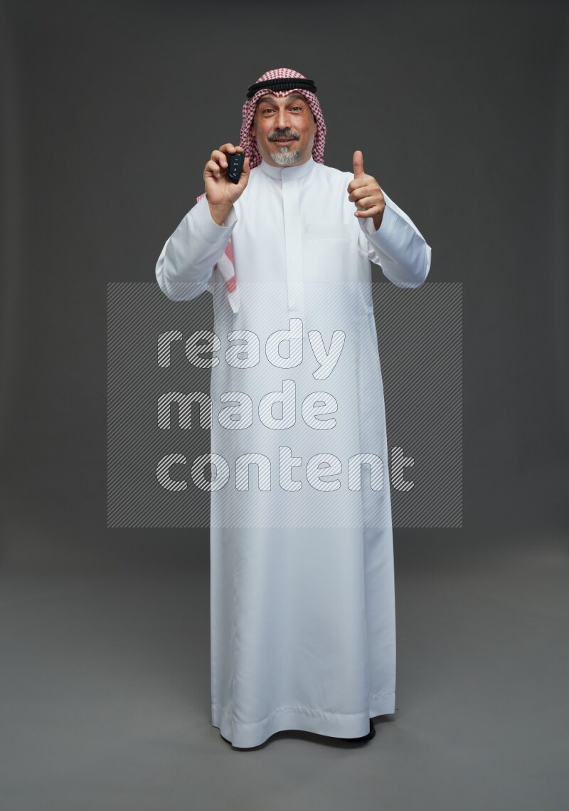 Saudi man with shomag Standing holding car key on gray background