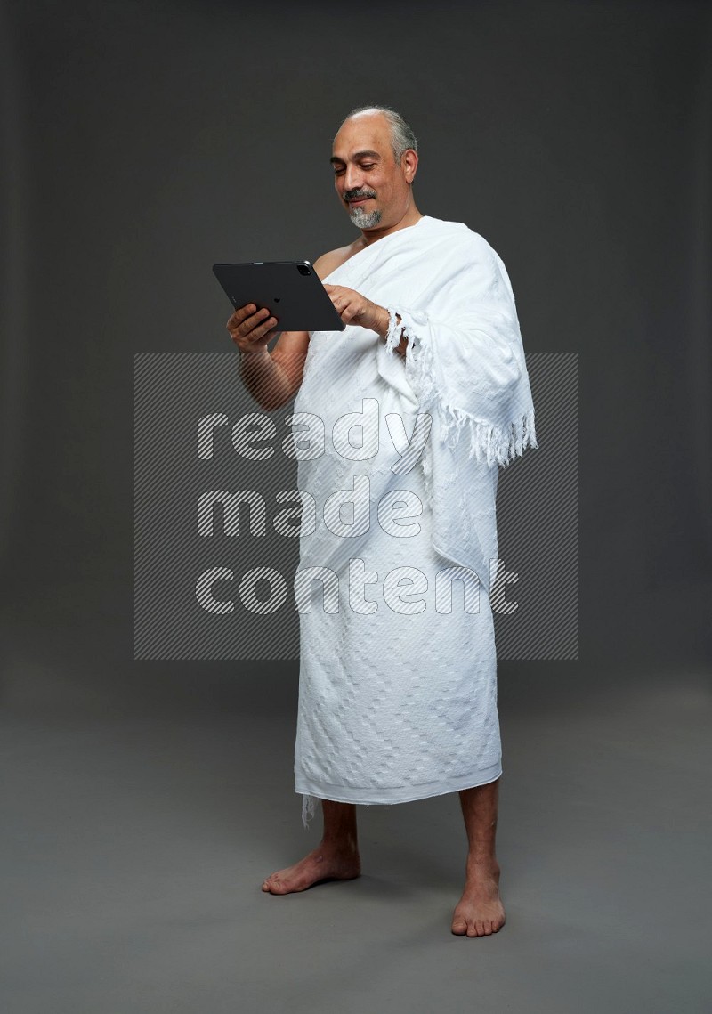 A man wearing Ehram Standing working on tablet on gray background