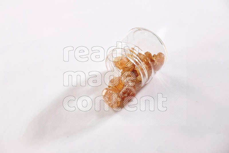 وعاء زجاجي ممتلئ بقطع الصمغ العربي والوعاء مقلوب وبعض القطع متناثرة خارجه علي خلفية بيضاء